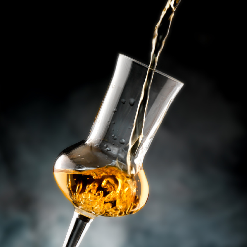 Bild zeigt das Einschenken eines holzgelagerten Grappas in ein stilvolles Grappaglas bei Miori in Saarbrücken. Das warme, goldene Licht, das durch den klaren Grappa scheint, kontrastiert wunderschön mit dem Glanz des Glases, was ein Gefühl von Qualität und Luxus vermittelt