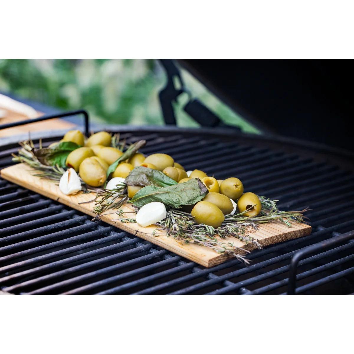Oliven, Knoblauch und Kräuter auf einer Grillplanke auf dem Big Green Egg
