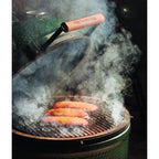 Hand streut Big Green Egg Hickory-Chips über die glühende Holzkohle im Grill