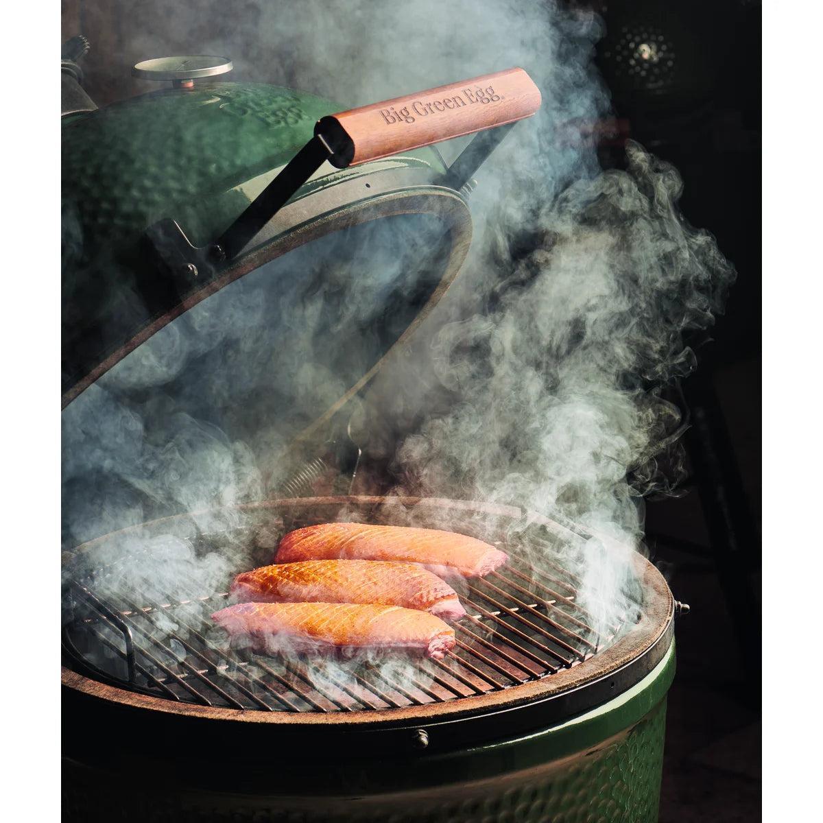 Hand streut Big Green Egg Hickory-Chips über die glühende Holzkohle im Grill