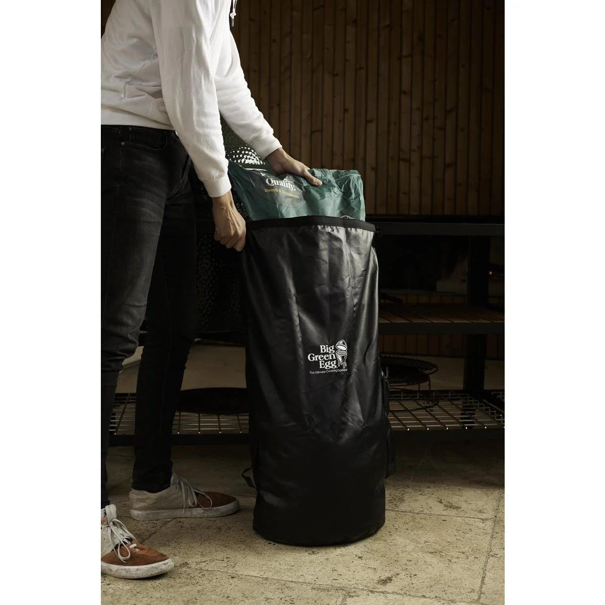 Person befüllt den schwarzen Big Green Egg Aufbewahrungsbeutel mit einem Sack Holzkohle.