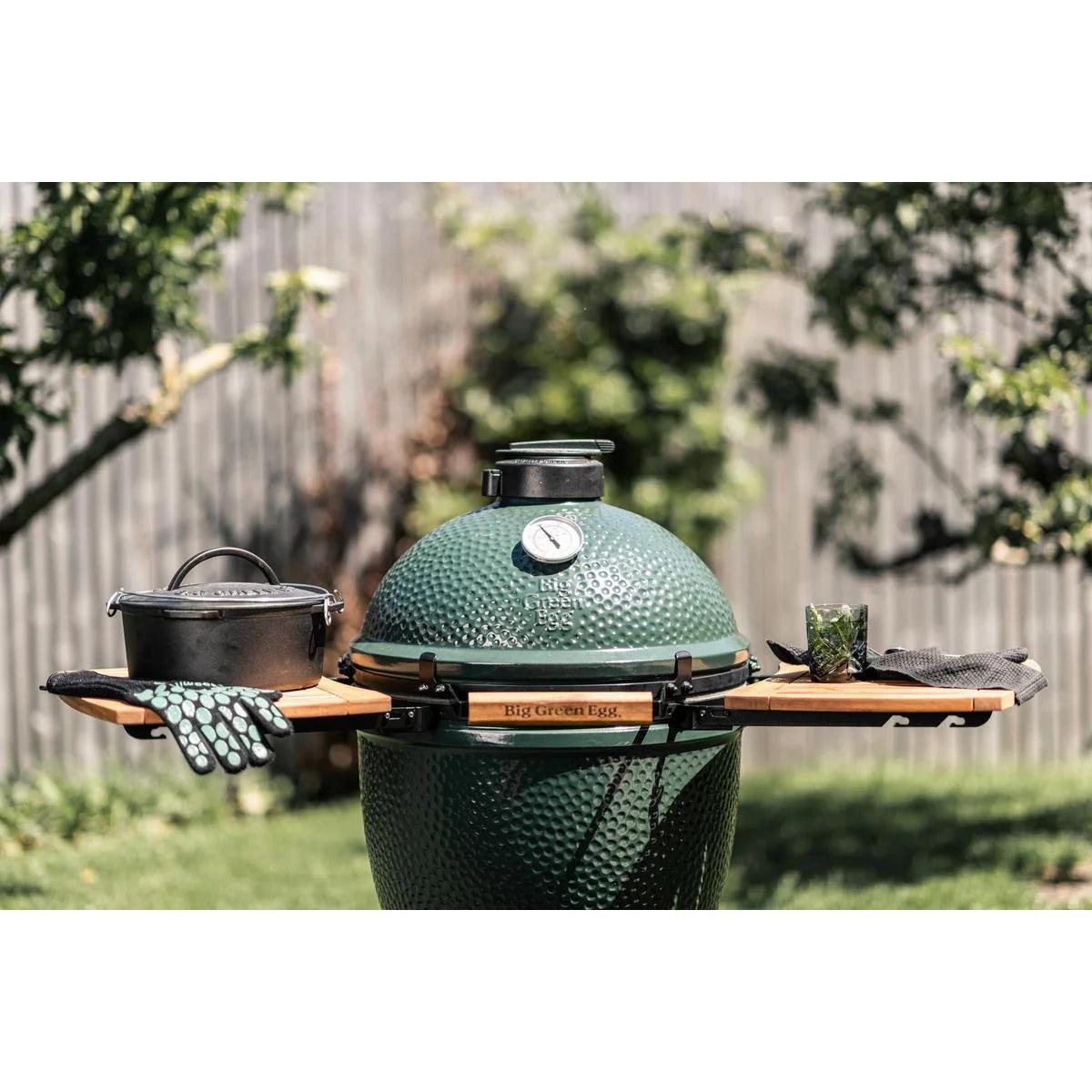 Big Green Egg mit zwei Akazien-Seitentischen, Gusseisentopf und Handschuhen im Garten