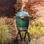 Big Green Egg Medium mit aufsteigendem Rauch auf schwarzem Gestell im herbstlichen Garten