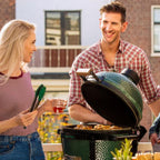 Paar grillt gemeinsam am geöffneten Big Green Egg MiniMax auf dem Balkon