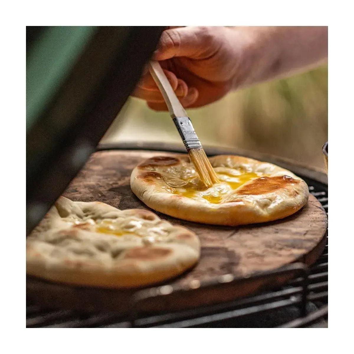 Zwei goldbraune Fladenbrote auf dem Big Green Egg Pizzastein L, eines wird mit Butter bepinselt.
