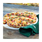Überbackene belegte Brotscheiben mit Tomaten und Käse auf dem Big Green Egg Pizzastein, daneben grünes Tuch.