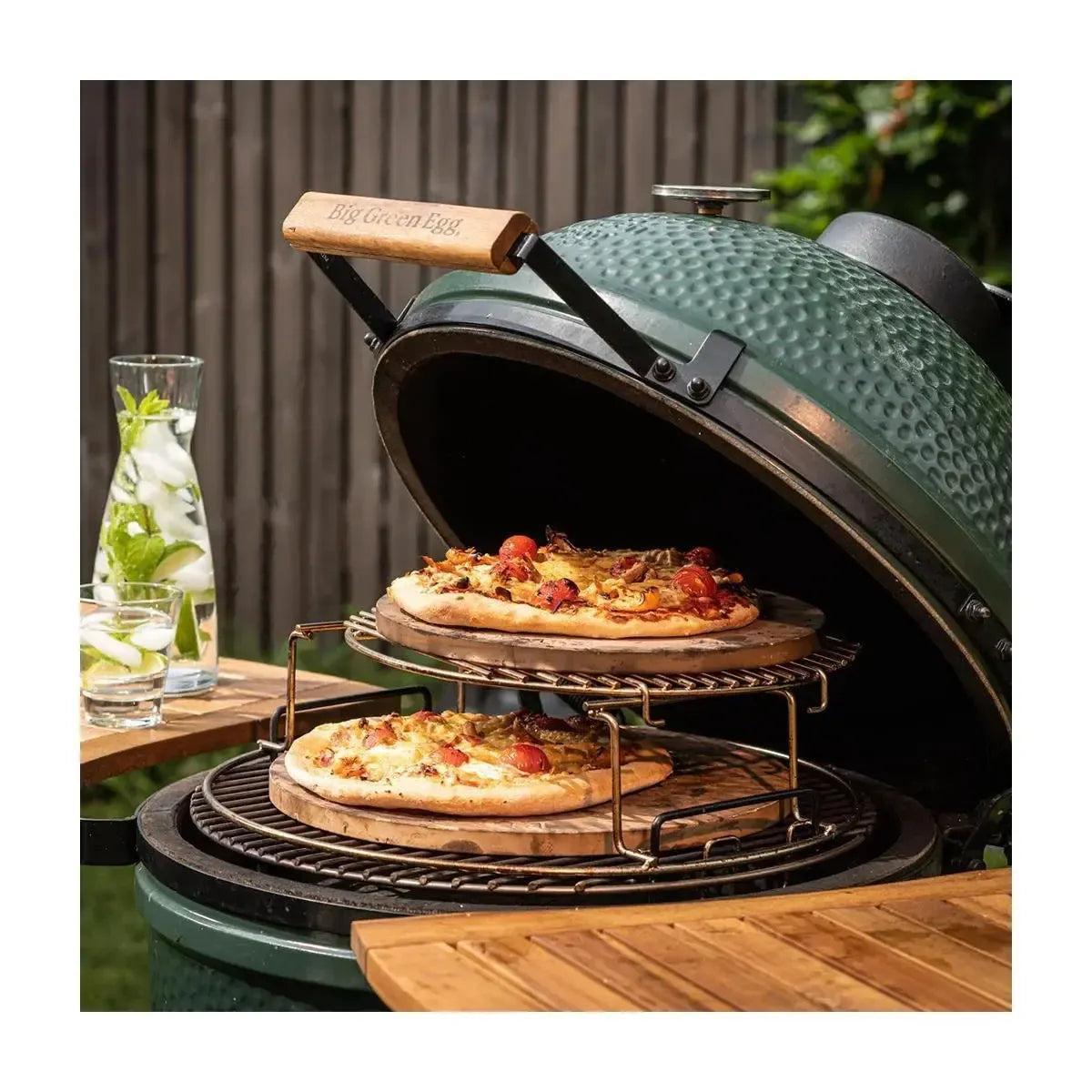 Zwei belegte Pizzen auf Big Green Egg Pizzasteinen, gestapelt im Rack über dem geöffneten Keramikgrill.
