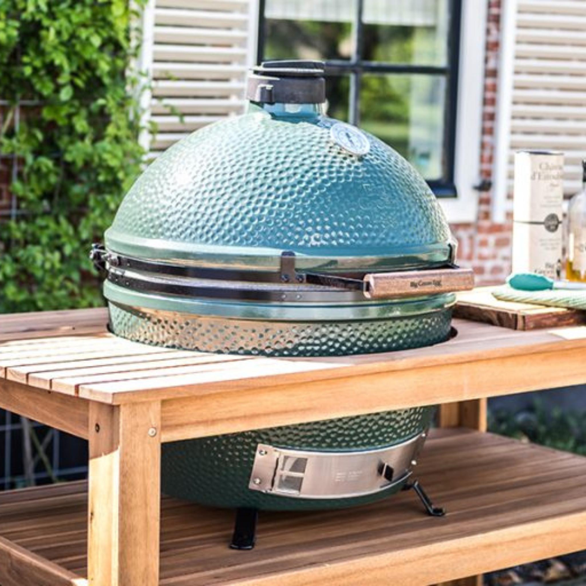 Big Green Egg XLarge auf einem Eukalyptustisch auf der Terrasse vor Backsteinwand