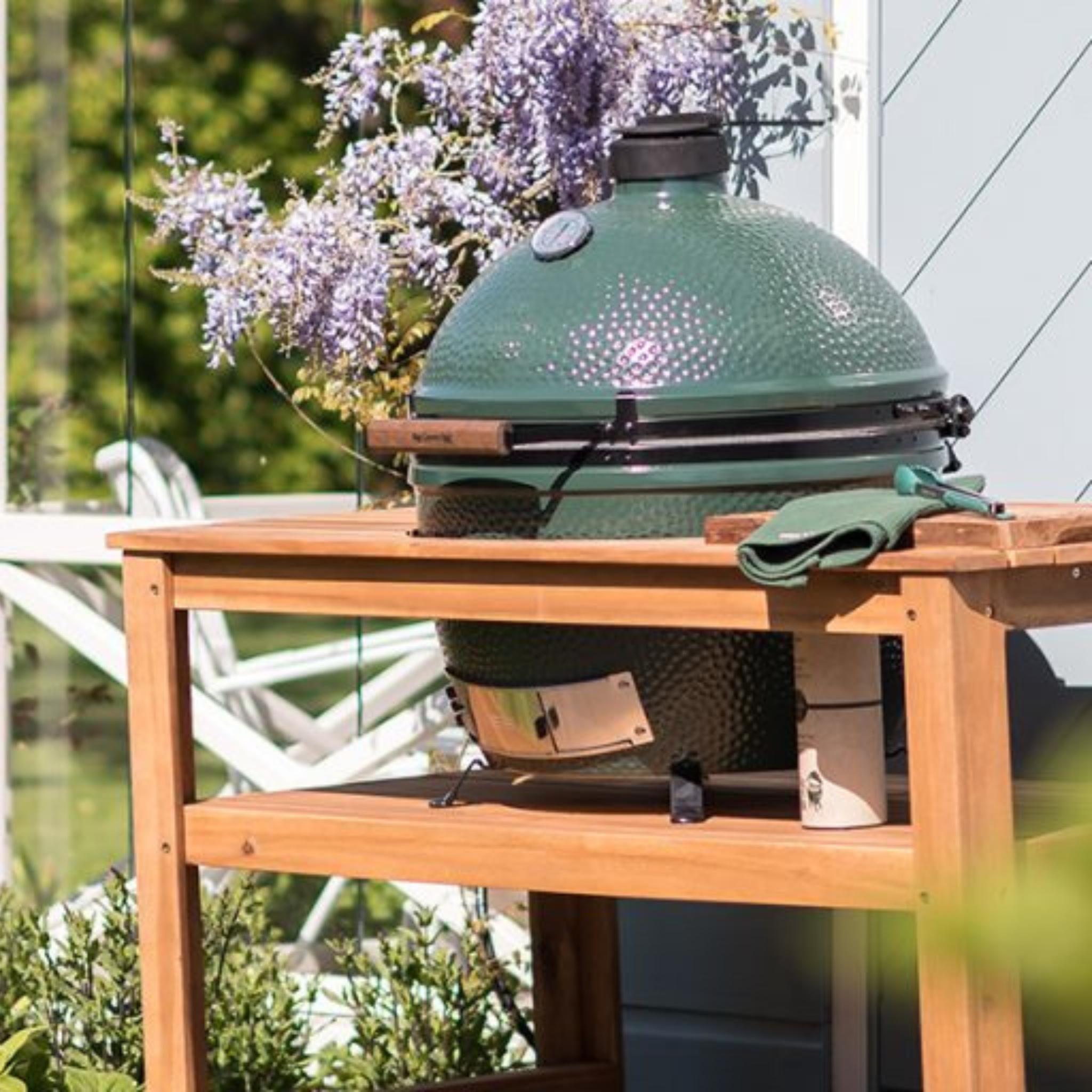 Big Green Egg XLarge auf Holztisch im Garten neben blühender Glyzinie