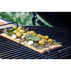 Grüne Oliven, Knoblauch und Kräuter auf einer Zedernholz-Grillplanke auf dem Big Green Egg