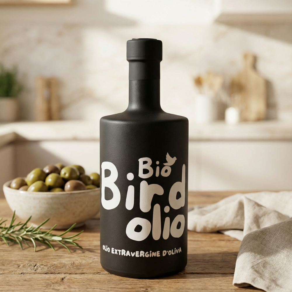 Schwarze Bio Birdolio Olivenölflasche auf Holztisch in heller Küche, daneben Schale mit grünen Oliven und Rosmarin