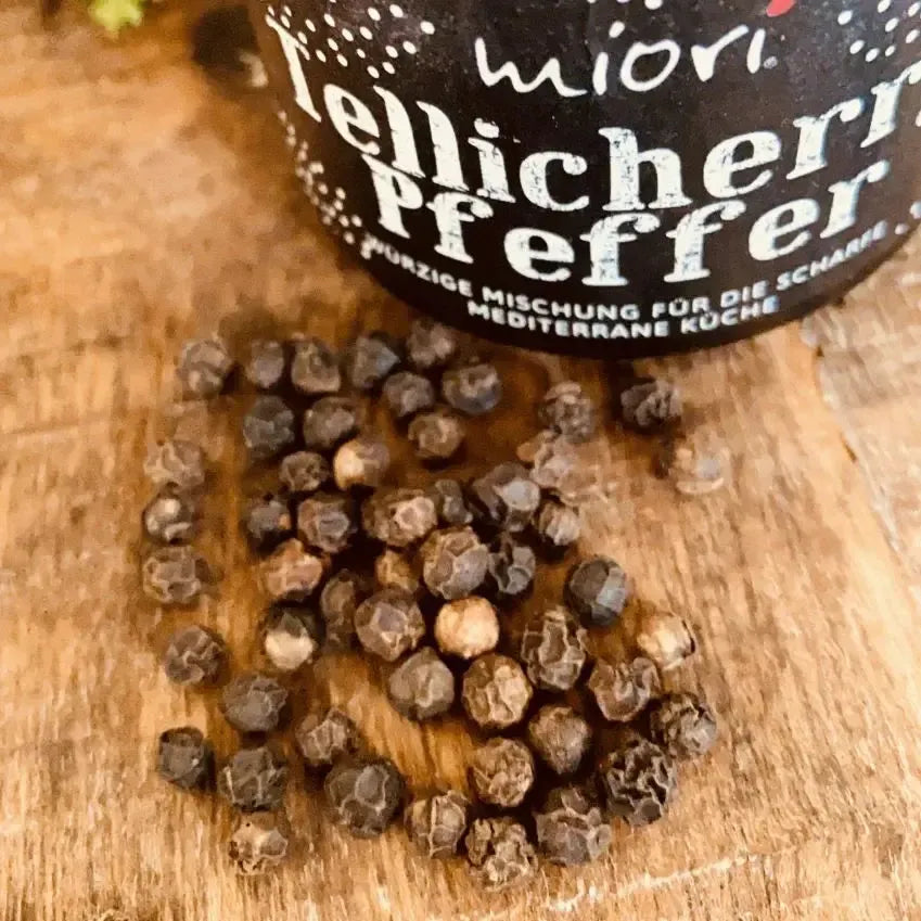 Nahaufnahme von aromatischen schwarzen Pfefferkörnern auf Holzbrett – hochwertige Gewürzspezialität aus dem Hause Miori Feinkost