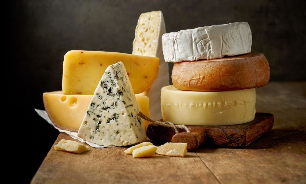 erschiedene Premium-Käsesorten: Blauschimmelkäse, Camembert und Hartkäse auf rustikalem Holzbre