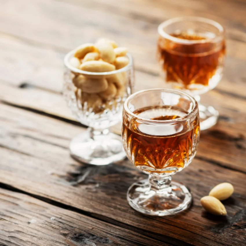 Elegante Liköre und Digestifs in kristallenen Gläsern mit Mandeln auf rustikalem Holztisch - miori süße Verführung Premium-Sortiment