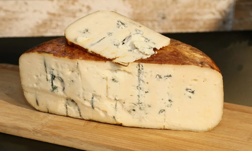 Keil eines cremigen Blauschimmelkäses mit feinen blauen Adern, aufgelegt auf einem Holzbrett.
