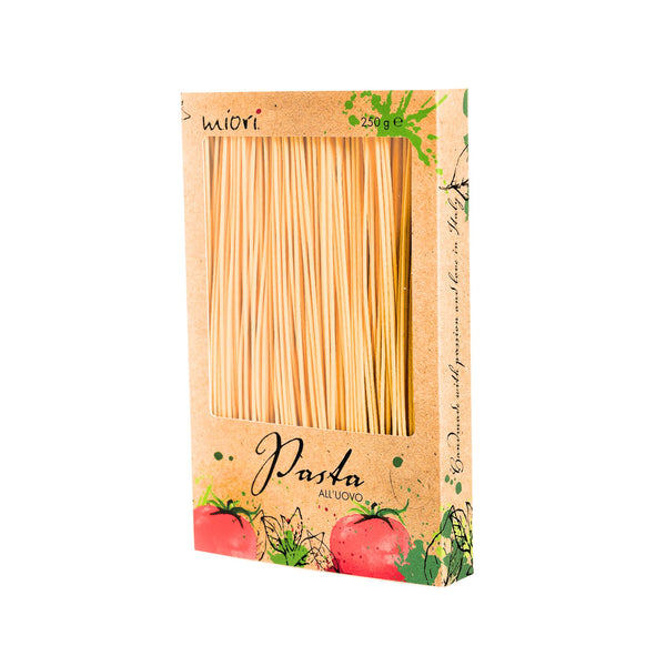 Eine rechteckige Pappschachtel mit einer transparenten Öffnung, durch die lange, dünne Nudelstränge sichtbar sind. Die Schachtel zeigt rote Tomaten-Illustrationen, grüne grafische Elemente und den Schriftzug „Pasta all’uovo“ sowie „Handmade with passion and love in Italy“
