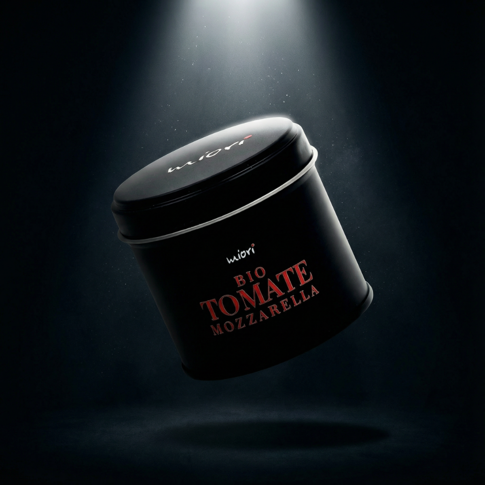 Schwarze Bio Tomate Mozzarella Gewürzdose von miori mit roter Schrift, schräg schwebend im Lichtkegel