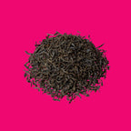Schüttbild Earl Grey Imperial, dunkle Schwarzteeblätter rund angeordnet auf pinkem Hintergrund