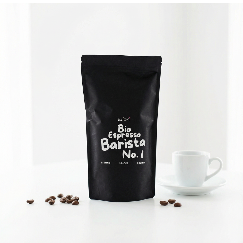 Bio Espresso Barista No. 1 Beutel vor weißem Hintergrund neben Espressotasse und verstreuten Kaffeebohnen