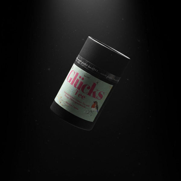 Glücks Tee Dose von miori mit mintgrünem Etikett und Rotkehlchen, schräg schwebend vor schwarzem Hintergrund