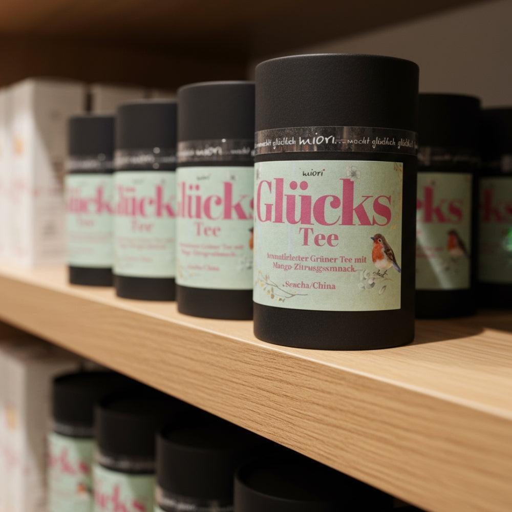 Glücks Tee Dosen in Reihe auf Holzregal präsentiert, vordere Dose scharf mit mintgrünem Etikett