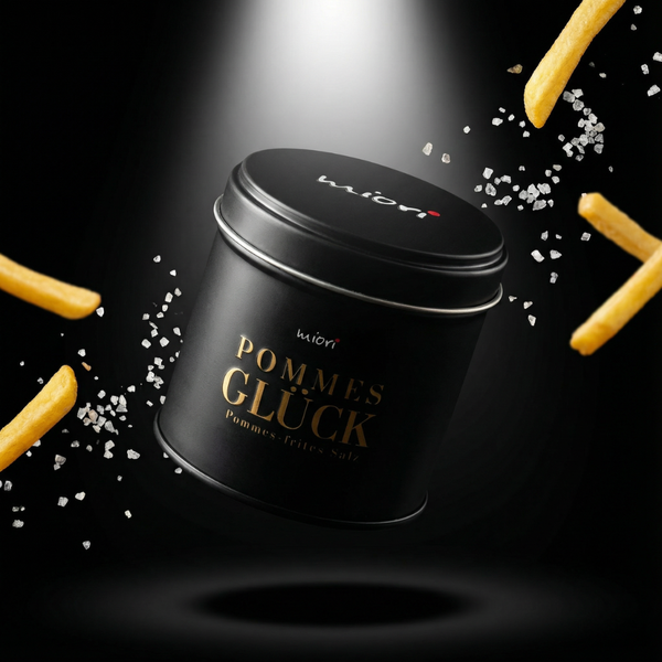 Schwarze Pommes Glück Gewürzsalz Dose von miori mit goldener Schrift, schwebend zwischen fliegenden Pommes und Salz