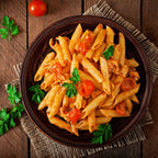 Teller Penne mit Tomatensauce und Kirschtomaten, garniert mit Petersilie, auf rustikalem Holztisch