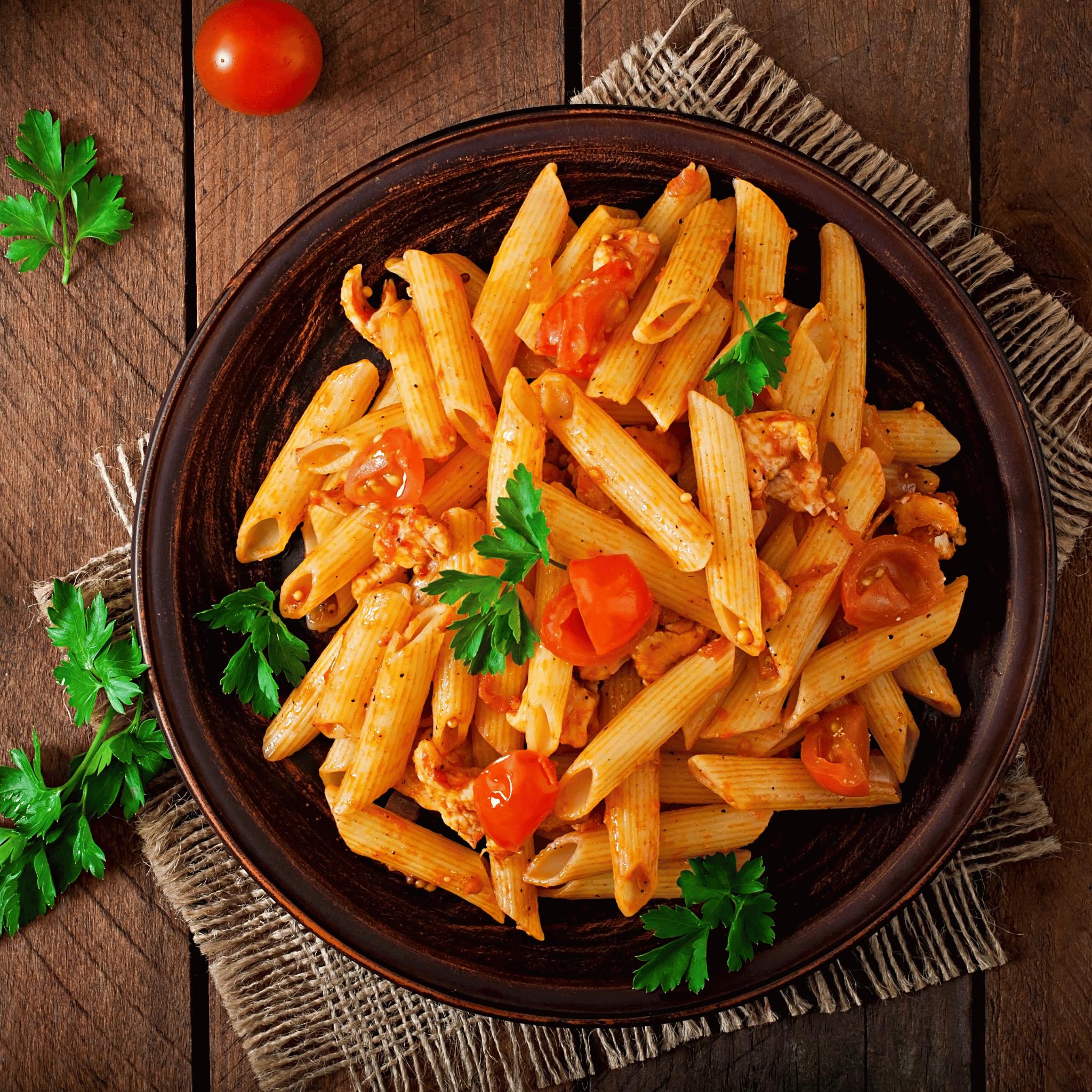 Teller Penne mit Tomatensauce und Kirschtomaten, garniert mit Petersilie, auf rustikalem Holztisch