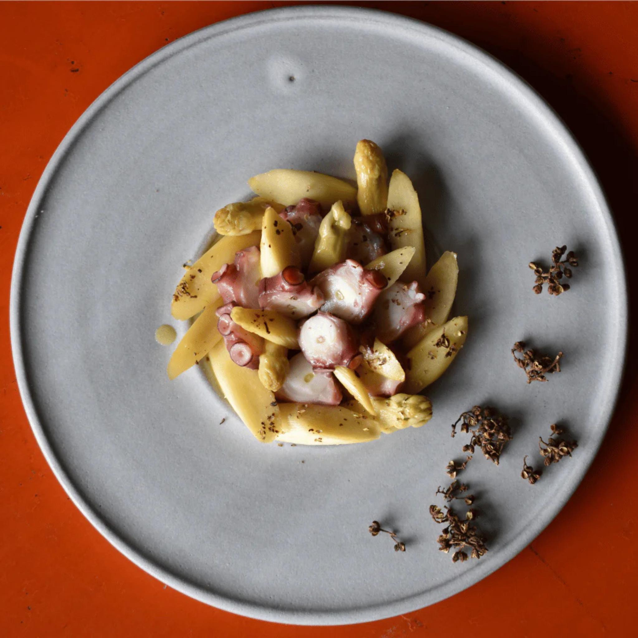 Pulpo mit weißem Spargel auf grauem Teller, dazu Andaliman-Beeren der Rosenheimer Gewürzmühle, oranger Hintergrund