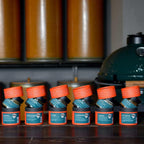 Reihe geöffneter orange Dosen der Rosenheimer Gewürzmühle vor grünem Big Green Egg Grill und Messing-Mühlen