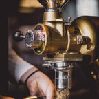 Nahaufnahme der Messing-Gewürzmühle Rosenheim beim Mahlen, frisch gemahlenes Gewürz rieselt aus dem Auslauf