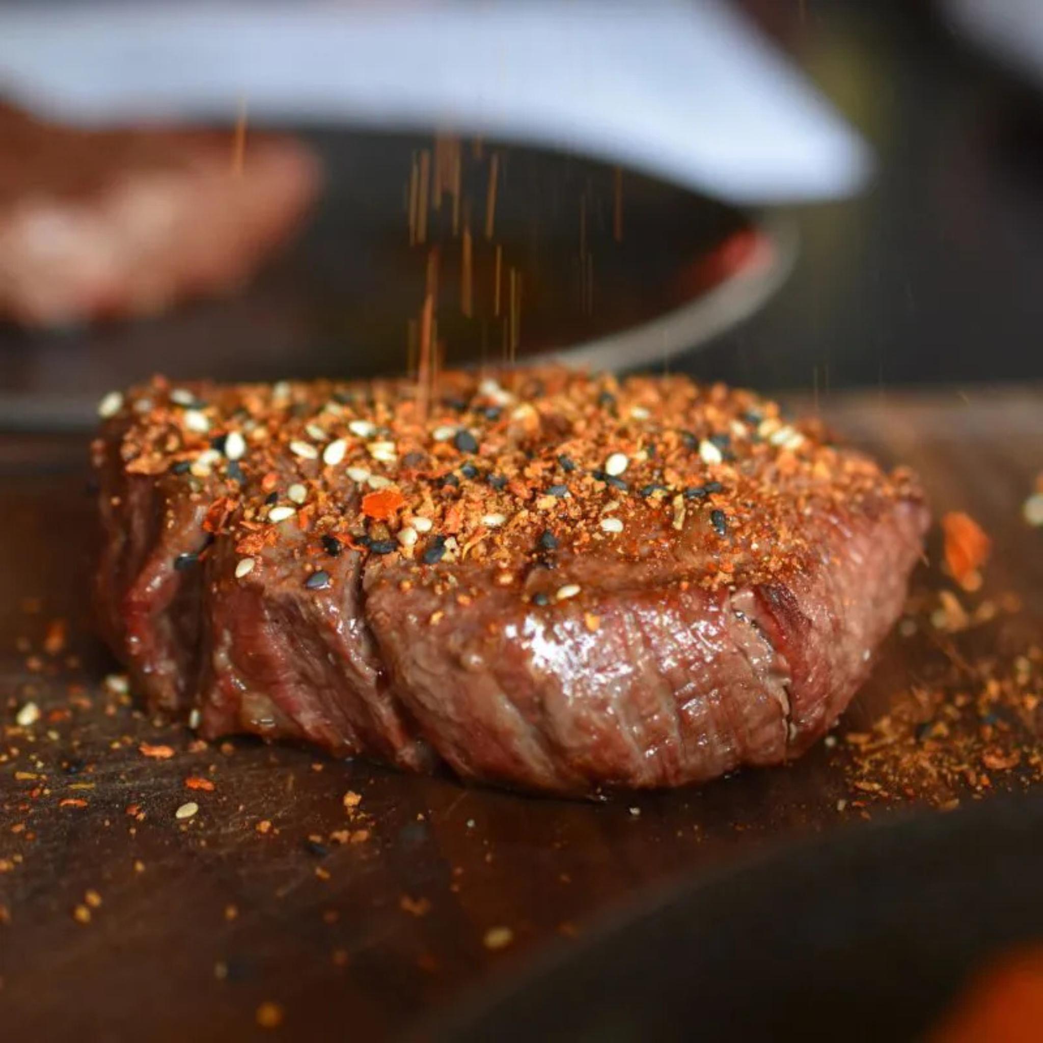 Dickes Steak auf Holzbrett wird mit Korean S(e)oul Rub aus Sesam und Chiliflocken bestreut