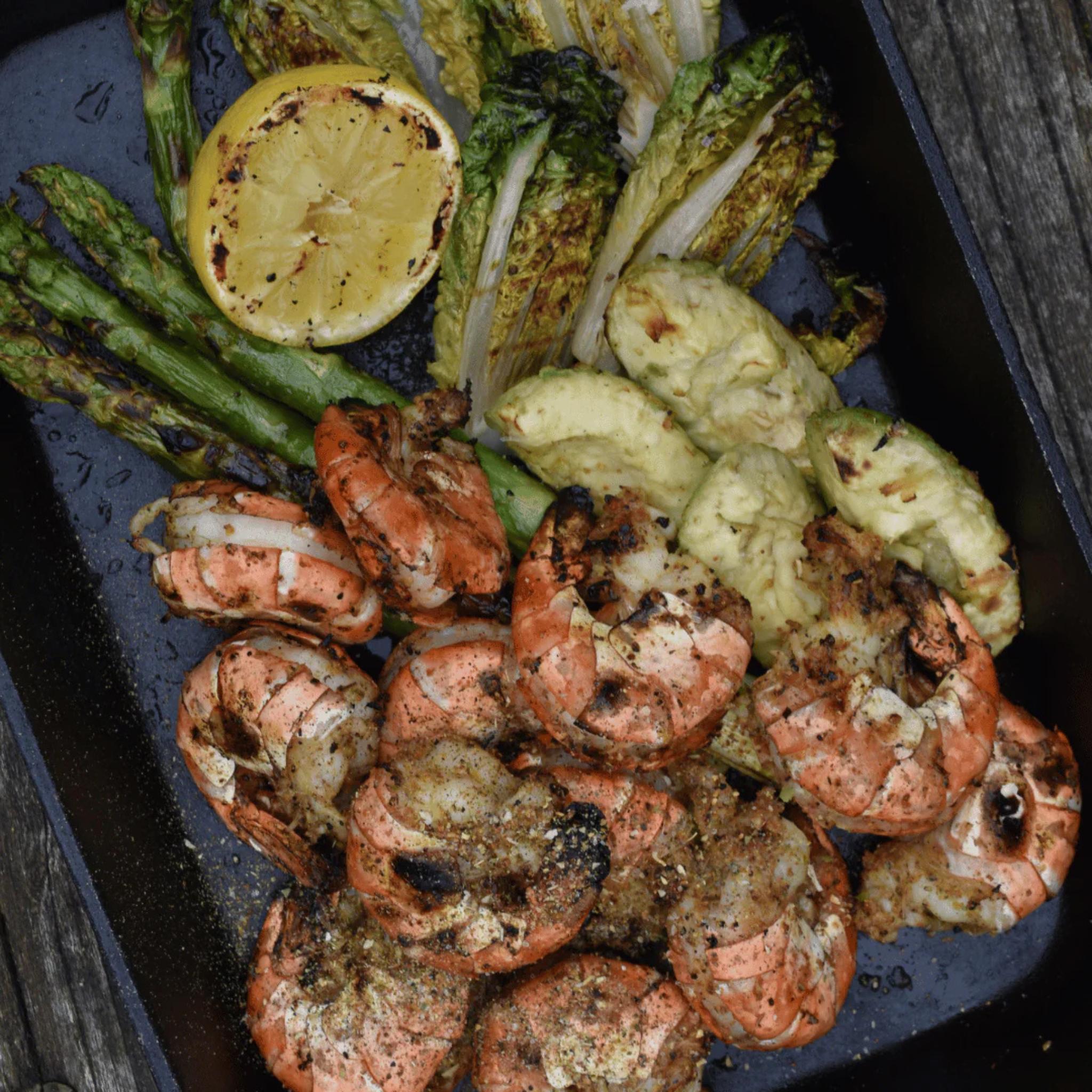 Gegrillte Garnelen mit gegrillter Zitrone, grünem Spargel und Avocado auf dunkler Gusseisenplatte, Orange Ocean Rub