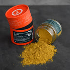 Orange Dose und gekipptes Glas Yuzu Curry auf dunklem Schiefer, leuchtend gelbes Currypulver ausgeschüttet