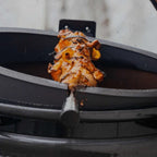 The Spit on Fire Large 21 Zoll im Einsatz, gegrilltes Fleisch am Edelstahl-Drehspieß über dem geöffneten Kugelgrill
