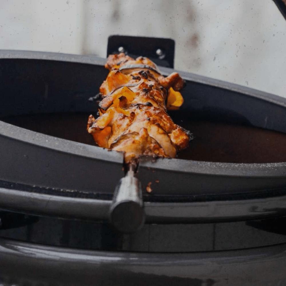 The Spit on Fire Large 21 Zoll im Einsatz, gegrilltes Fleisch am Edelstahl-Drehspieß über dem geöffneten Kugelgrill