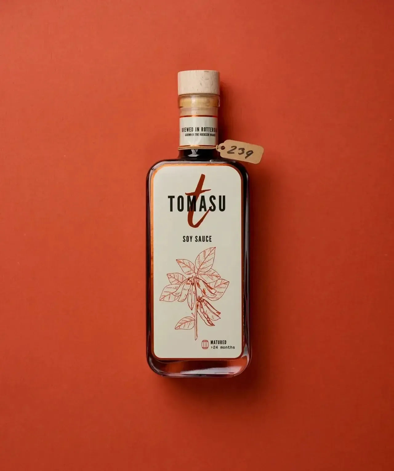 Tomasu Premium-Sojasauce 200 ml in der Glasflasche mit Holzkorken, liegend auf rostrotem Hintergrund – über 24 Monate gereift