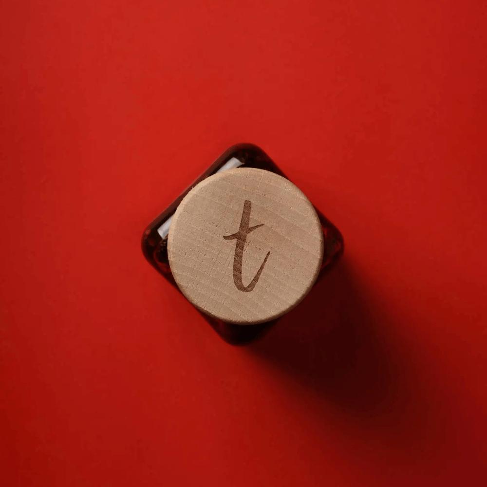 Holzdeckel des Tomasu-Sambal-Glases mit eingraviertem t-Logo, von oben auf rotem Hintergrund