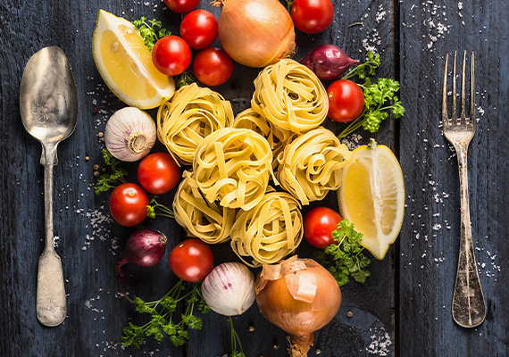 Schön arrangierte Pasta mit Tomaten, Zwiebeln und Kräutern auf einem schwarzen Holztisch und Silberbesteck bei miori