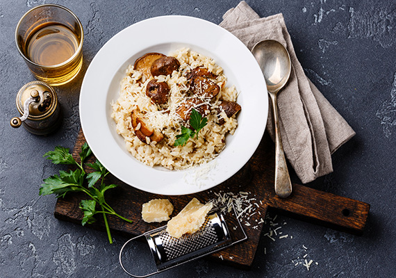 Risotto mit Pilzen und Trüffel in einem weissen Teller arrangiert mit einer Parmesanreibe auf dunklem Untergrund bei miori