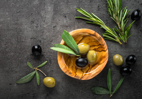 Olivenholzschale mit grünen und schwarzen Olivem und Olivenblatt auf dunkler Arbeitsplatte bei miori