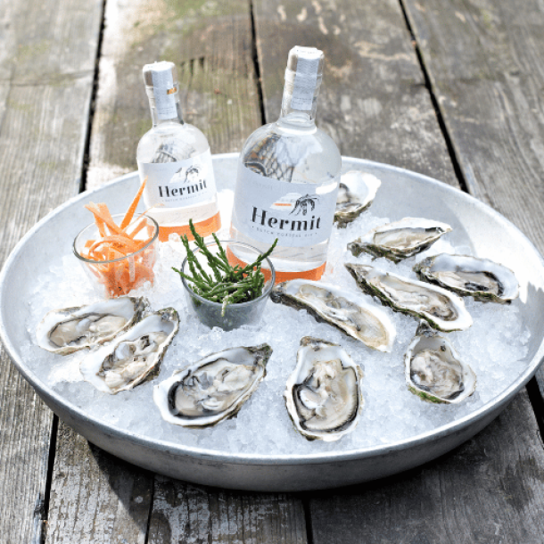 Flasche Hermit Gin auf einem Tisch neben einer Portion frischer Austern, perfekt präsentiert für einen stilvollen und delikaten Genuss.