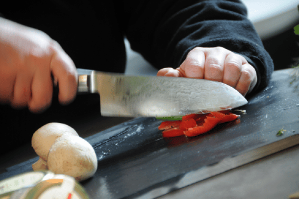 Gemüse wird auf schwarzem Brett mit japanischem Messer geschnitten - präsentiert im miori Messersortiment