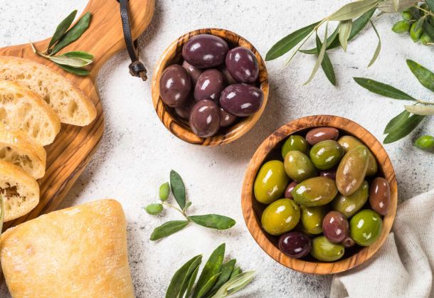 Vielfältiges Sortiment an Oliven von der Miori Antipasti-Frischetheke, präsentiert in Holzschälchen mit frischem Brot und Olivenzweigen