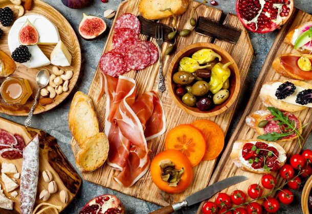 Bunte Auswahl an Miori-Antipasti auf rustikalen Holzbrettern arrangiert, einschließlich Salami, Schinken, Käse, Oliven, Feigen, und frischem Brot.